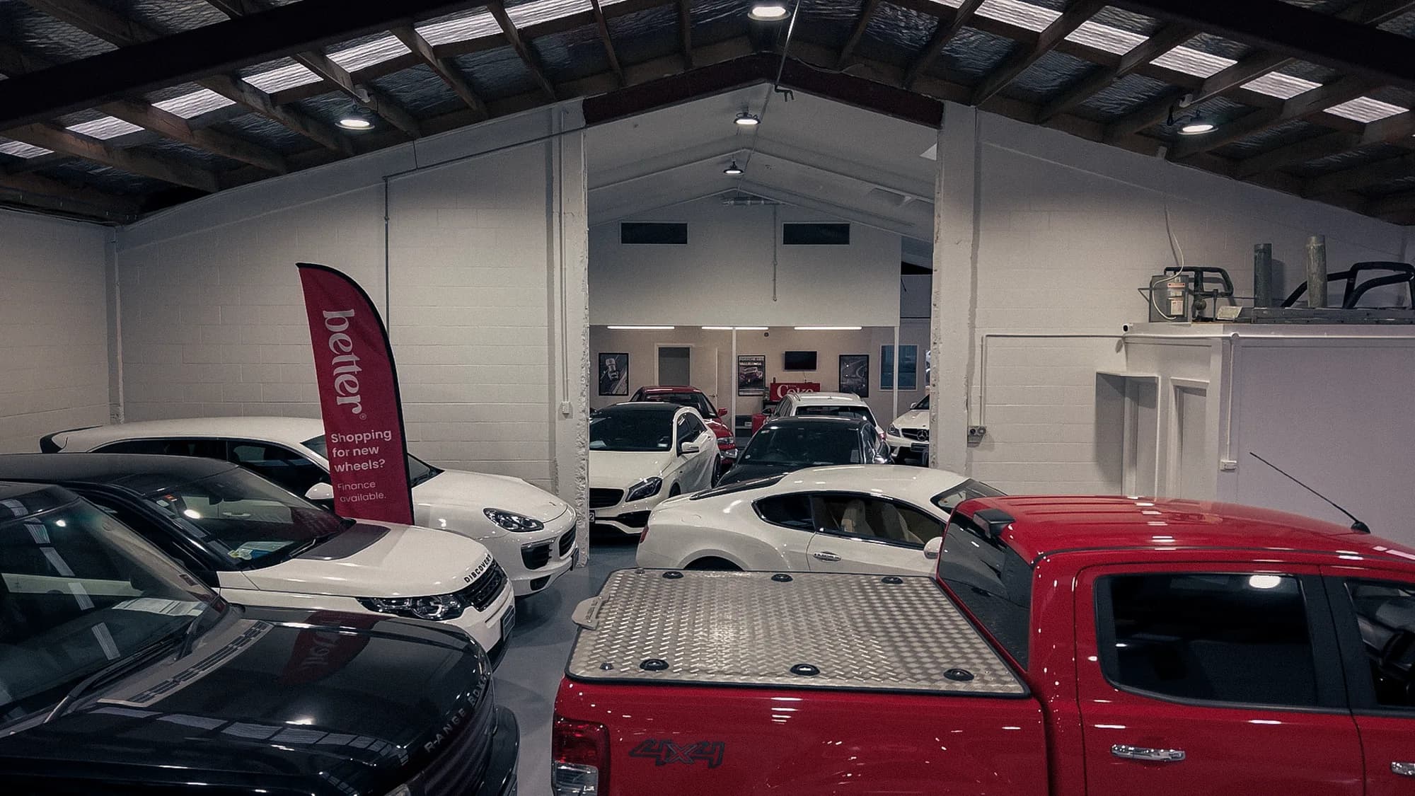 Indoor showroom floor with Range Rover, Porsche and pickup at Auto Luxe