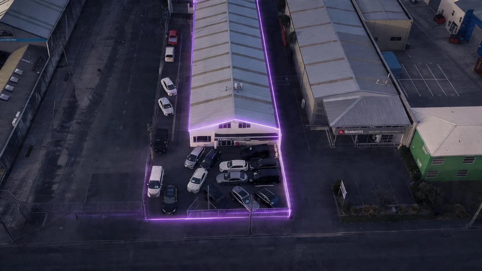 Premium Wholesale Cars Christchurch dealership exterior at dusk with a cloudless indigo to rose gradient sky, warm amber interior light glowing from showroom windows and upstairs offices, and the brand purple car icon and signage illuminated